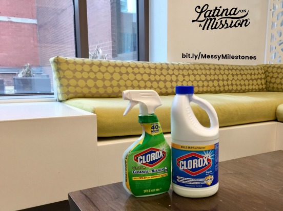 Clorox products on a brown table, in front of a green & white sofa. A window is behind the sofa. 