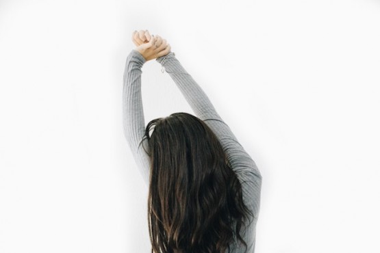 Woman with long black hair stretching arms above her head.