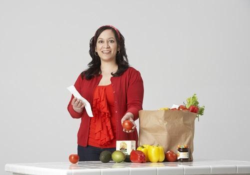 Shown: Migdalia Rivera standing in front of a table, taking out heart healthy foods from a brown paper bag.