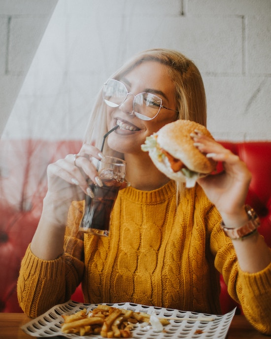 woman-eating-burger-drinking-soda-unsplash