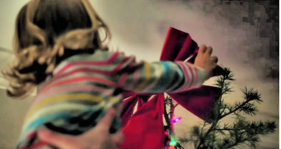 Little girl putting a star on the top of a Christmas tree.