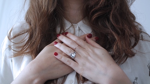 Shown: Woman with long hair clasping her hands in front of her heart.